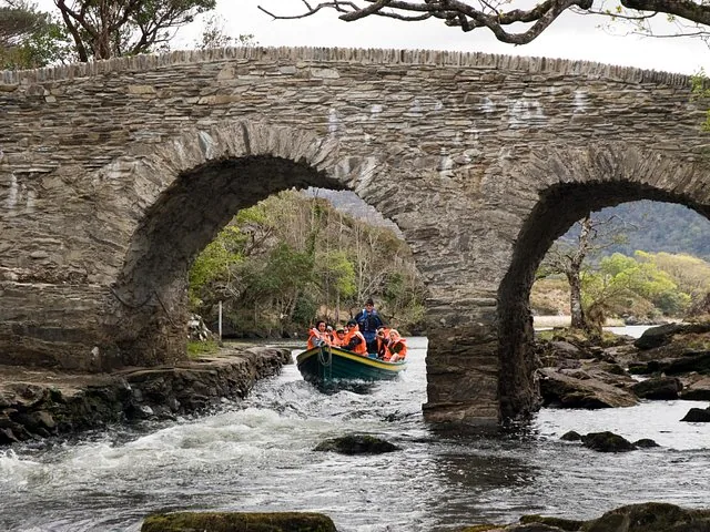 Small boat with tourists passing under an old stone bridge with two arches