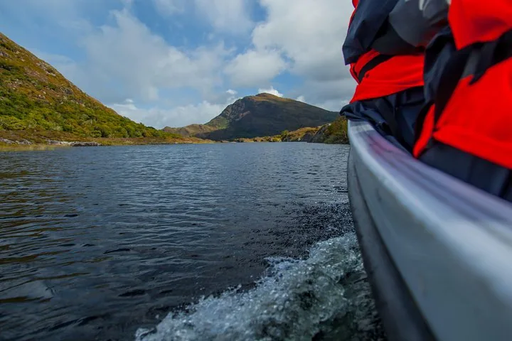 View from inside a moving boat showing lake, distant mountains, and passenger in orange lifejacket