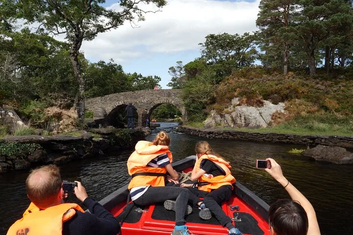 Passengers on a red boat taking photos of a stone arched bridge over a river