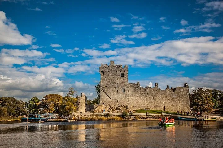Small green boat carrying tourists on a lake with Ross Castle in the background