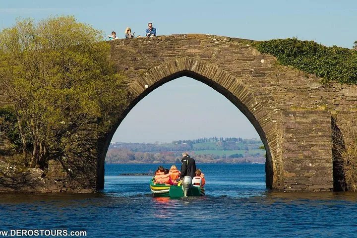Boat with passengers in life jackets passing under a stone arch bridge on water